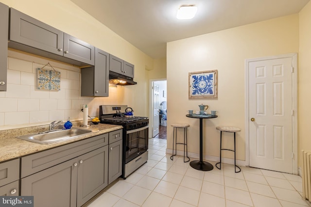 kitchen featuring stainless steel gas range oven, gray cabinets, under cabinet range hood, a sink, and backsplash