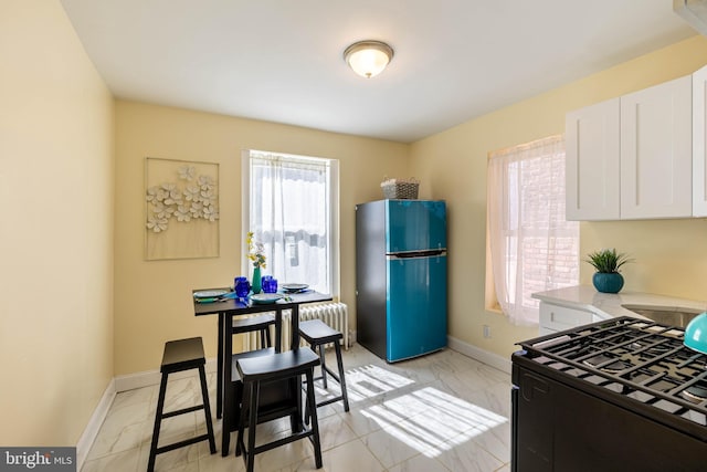 kitchen with radiator heating unit, black gas stove, white cabinetry, freestanding refrigerator, and baseboards