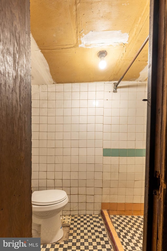 bathroom featuring a shower stall, toilet, and tile walls