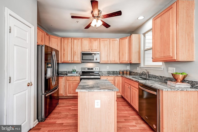 kitchen featuring a center island, light brown cabinetry, light wood-style flooring, appliances with stainless steel finishes, and a sink