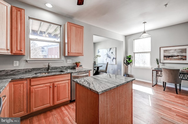 kitchen with a sink, light wood-type flooring, stainless steel dishwasher, and dark stone countertops