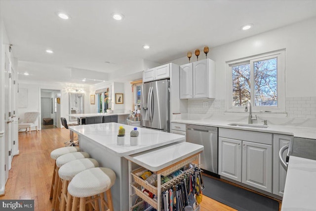 kitchen with light wood-type flooring, a sink, a kitchen breakfast bar, a kitchen island, and appliances with stainless steel finishes