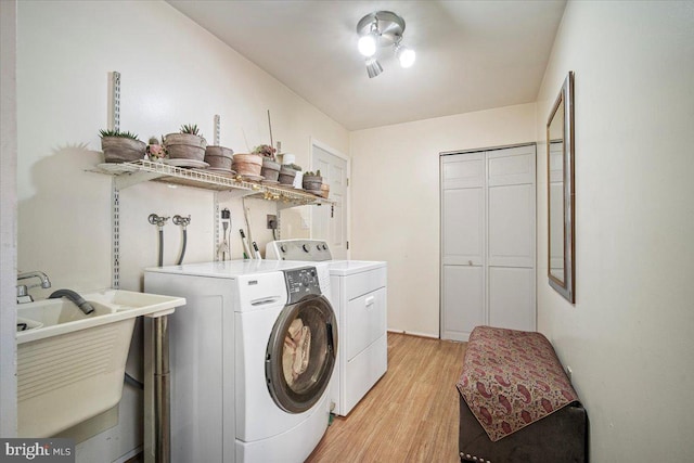 washroom featuring laundry area, separate washer and dryer, light wood-style floors, and a sink