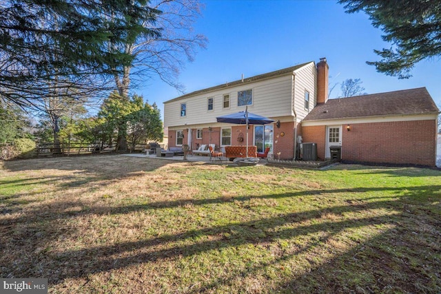 rear view of house featuring central AC unit, a yard, a chimney, a patio area, and brick siding