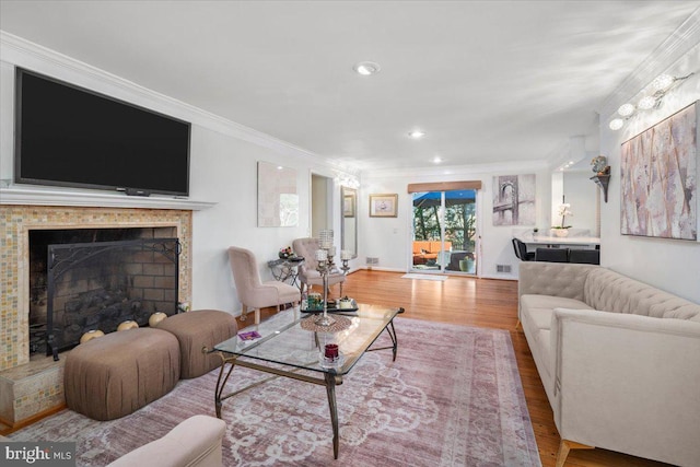 living area with visible vents, a fireplace with raised hearth, crown molding, recessed lighting, and wood finished floors