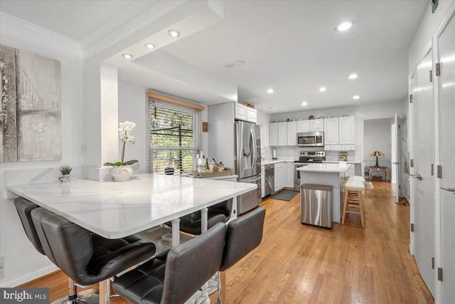 kitchen with recessed lighting, appliances with stainless steel finishes, a kitchen breakfast bar, light wood-style floors, and white cabinetry