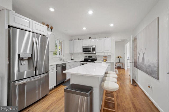 kitchen featuring decorative backsplash, appliances with stainless steel finishes, a kitchen breakfast bar, white cabinets, and a sink