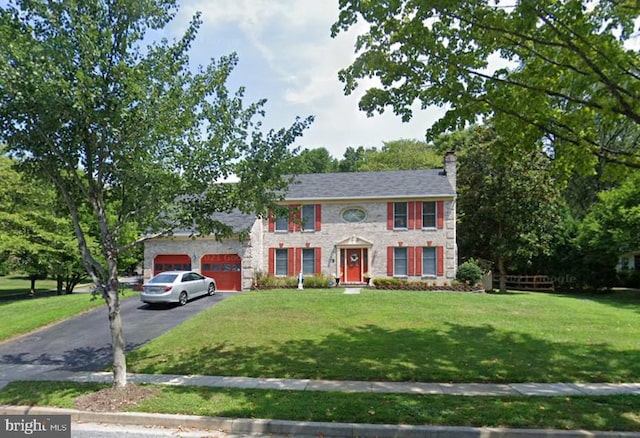 colonial home featuring aphalt driveway, a front yard, a chimney, and an attached garage