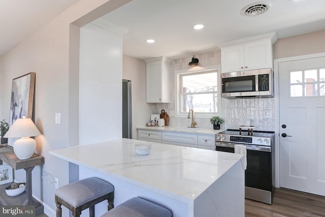 kitchen featuring visible vents, a sink, decorative backsplash, appliances with stainless steel finishes, and white cabinetry