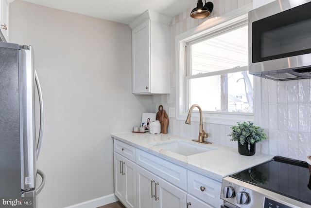 kitchen featuring a sink, tasteful backsplash, appliances with stainless steel finishes, white cabinets, and baseboards