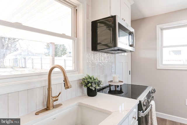 kitchen featuring baseboards, light countertops, white cabinets, stainless steel appliances, and a sink