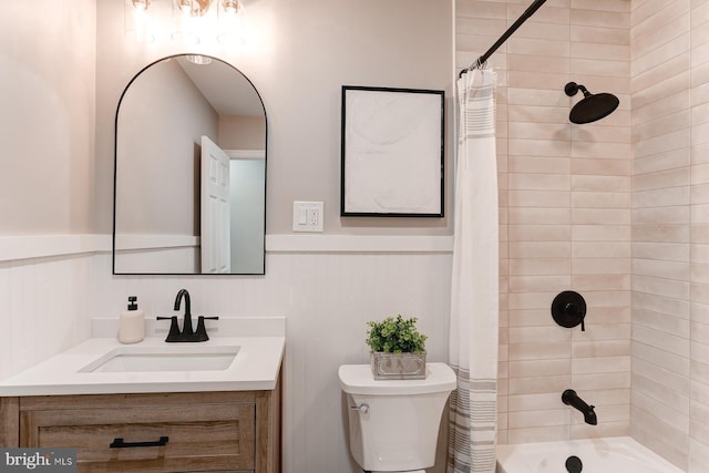 bathroom with vanity, toilet, shower / bathtub combination with curtain, and a wainscoted wall