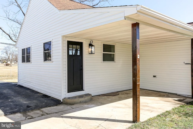 view of exterior entry with a carport and roof with shingles