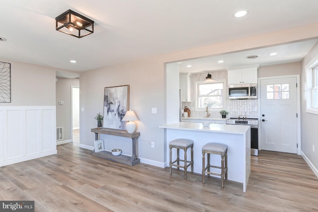 kitchen with stainless steel appliances, light wood-style flooring, white cabinets, and light countertops