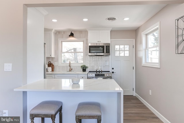 kitchen featuring a sink, a kitchen breakfast bar, tasteful backsplash, white cabinetry, and stainless steel appliances