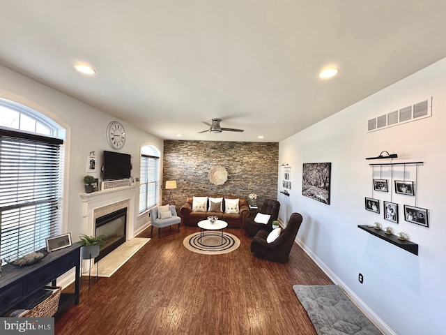 living area featuring wood finished floors, visible vents, baseboards, a high end fireplace, and ceiling fan