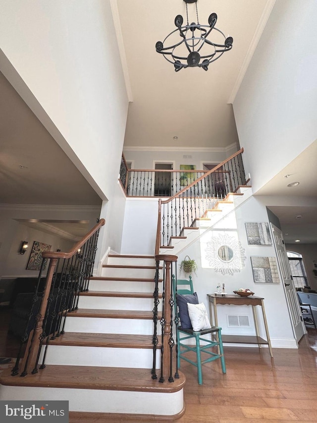 stairs featuring wood finished floors, visible vents, a towering ceiling, and ornamental molding