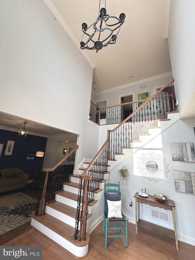 stairway featuring wood finished floors, visible vents, a high ceiling, crown molding, and a notable chandelier