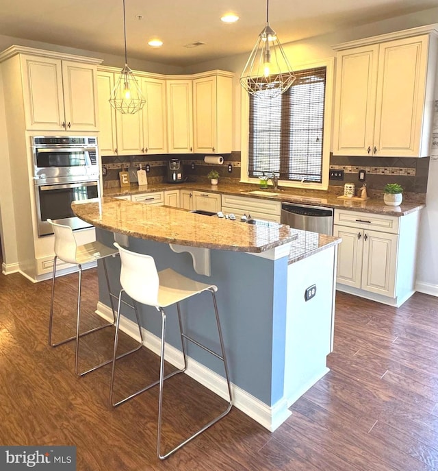 kitchen featuring light stone counters, dark wood finished floors, hanging light fixtures, appliances with stainless steel finishes, and a center island