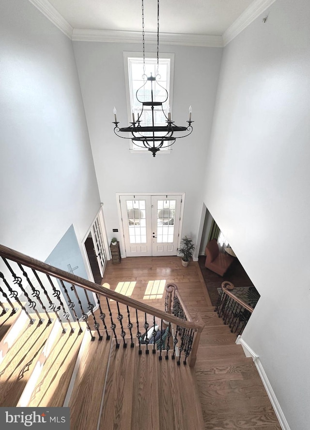 stairway with french doors, wood finished floors, and crown molding