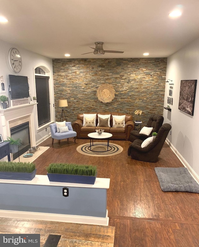 living area featuring a glass covered fireplace, baseboards, a ceiling fan, and wood finished floors