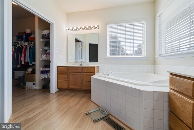 bathroom featuring vanity, wood finished floors, visible vents, a walk in closet, and a bath