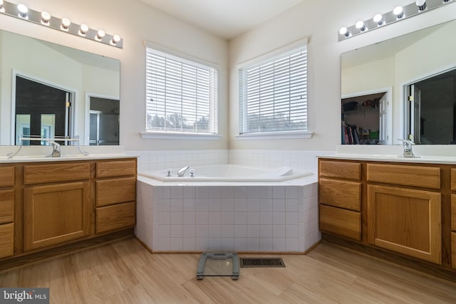 bathroom featuring a bath, wood finished floors, a stall shower, and a sink