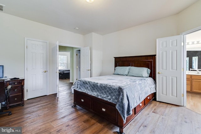 bedroom with ensuite bath, light wood-style floors, visible vents, and a sink