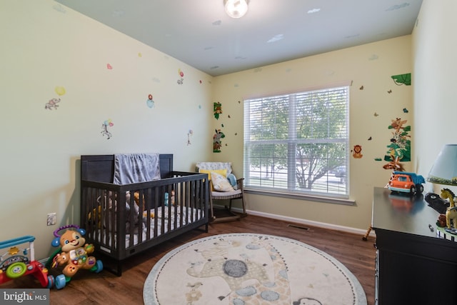 bedroom with a nursery area, wood finished floors, visible vents, and baseboards