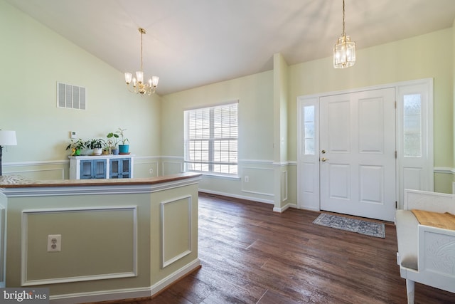 foyer entrance with a notable chandelier, dark wood-type flooring, visible vents, and vaulted ceiling