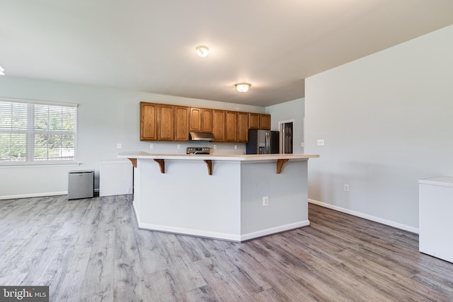 kitchen with light countertops, a kitchen bar, light wood-style flooring, appliances with stainless steel finishes, and brown cabinetry