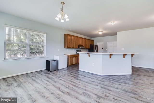 kitchen with a breakfast bar area, light countertops, brown cabinets, freestanding refrigerator, and light wood-style floors