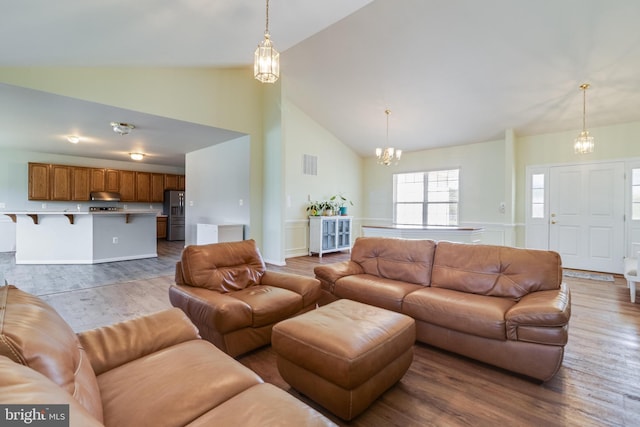 living area with visible vents, wood finished floors, high vaulted ceiling, and a chandelier