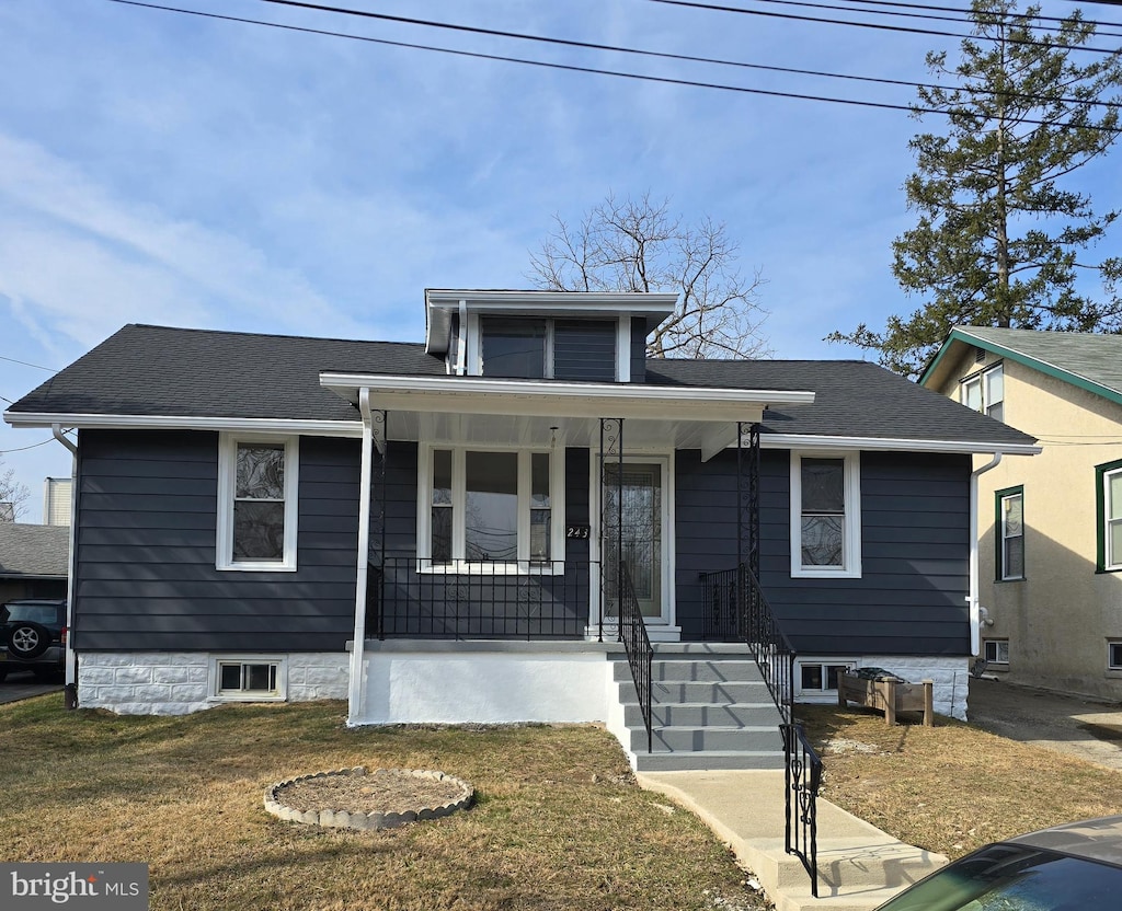 bungalow-style home featuring covered porch, a shingled roof, and a front lawn