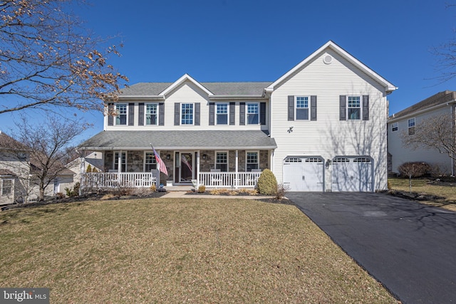 traditional home with aphalt driveway, a front yard, covered porch, a garage, and stone siding