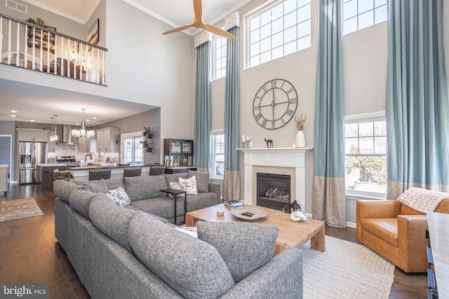 living area with visible vents, a premium fireplace, an inviting chandelier, dark wood-type flooring, and crown molding