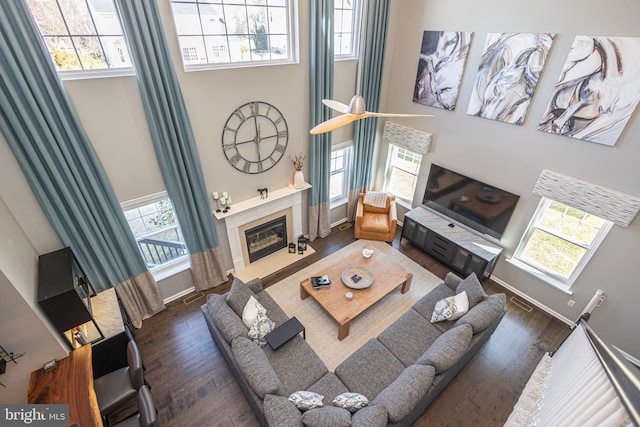 living area featuring a tile fireplace, baseboards, a towering ceiling, and wood finished floors