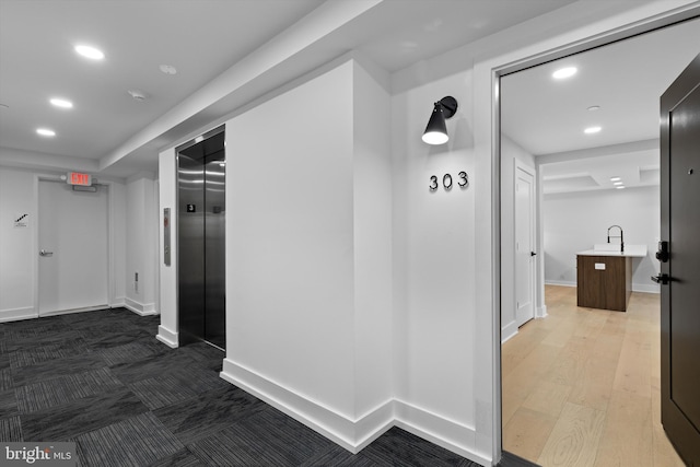 hall featuring wood finished floors, baseboards, elevator, recessed lighting, and a sink