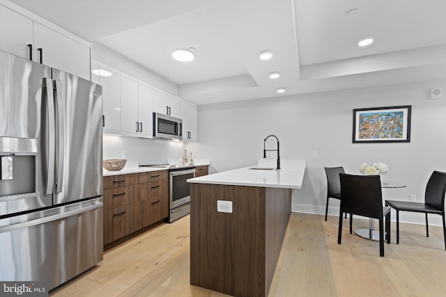 kitchen featuring light wood-type flooring, light countertops, appliances with stainless steel finishes, white cabinets, and a sink