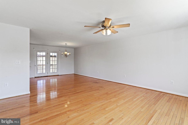 spare room with ceiling fan with notable chandelier, light wood-type flooring, and baseboards