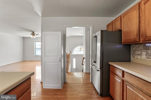 kitchen featuring light wood finished floors, backsplash, brown cabinetry, and freestanding refrigerator