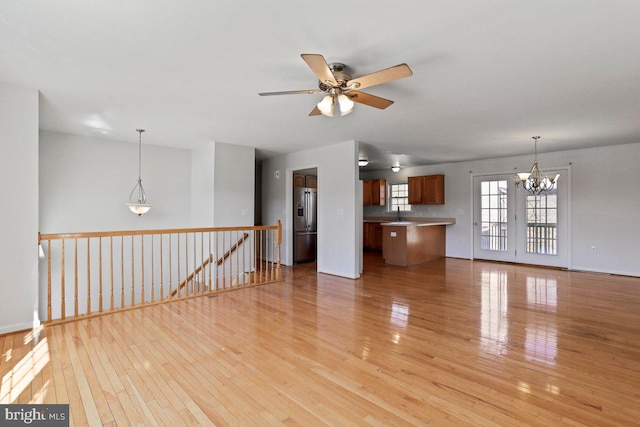 unfurnished living room featuring a sink, light wood-type flooring, and ceiling fan with notable chandelier