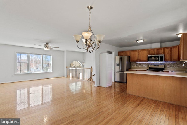 kitchen with light wood finished floors, a sink, decorative backsplash, stainless steel appliances, and open floor plan