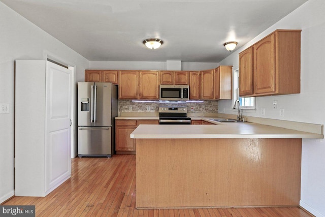 kitchen featuring light countertops, light wood-style flooring, a peninsula, stainless steel appliances, and a sink