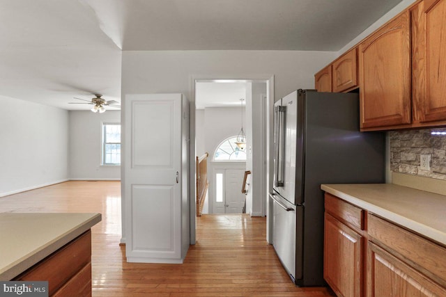 kitchen featuring decorative backsplash, brown cabinets, freestanding refrigerator, and light wood-style floors