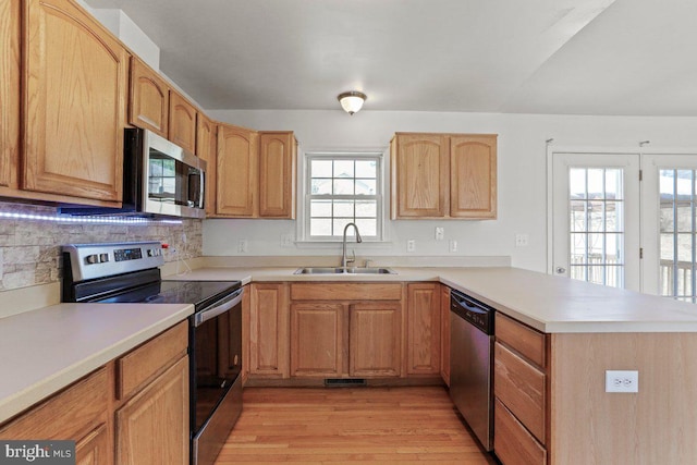 kitchen with a sink, appliances with stainless steel finishes, a peninsula, light wood finished floors, and light countertops