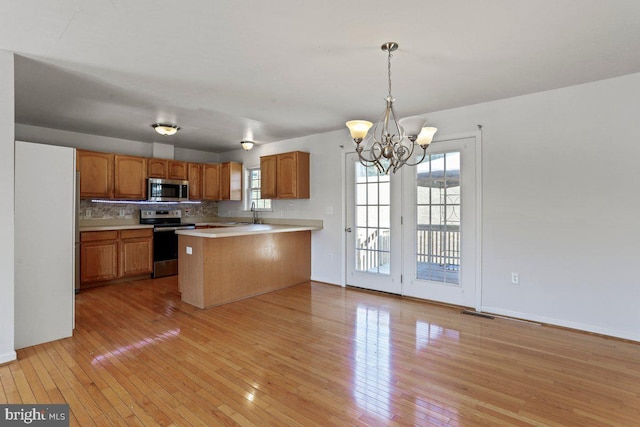 kitchen with light wood finished floors, tasteful backsplash, light countertops, appliances with stainless steel finishes, and a peninsula