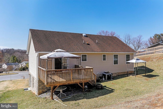 rear view of house with central air condition unit, roof with shingles, a gazebo, a lawn, and a deck