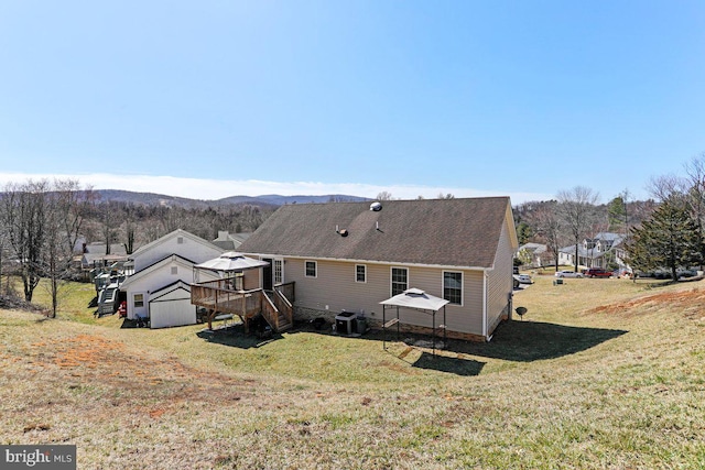 back of house with a deck with mountain view, a yard, and roof with shingles