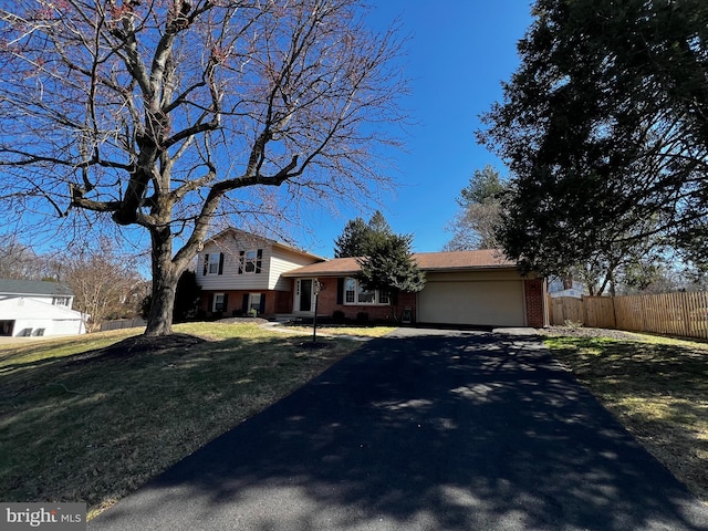 split level home featuring a front lawn, aphalt driveway, fence, an attached garage, and brick siding